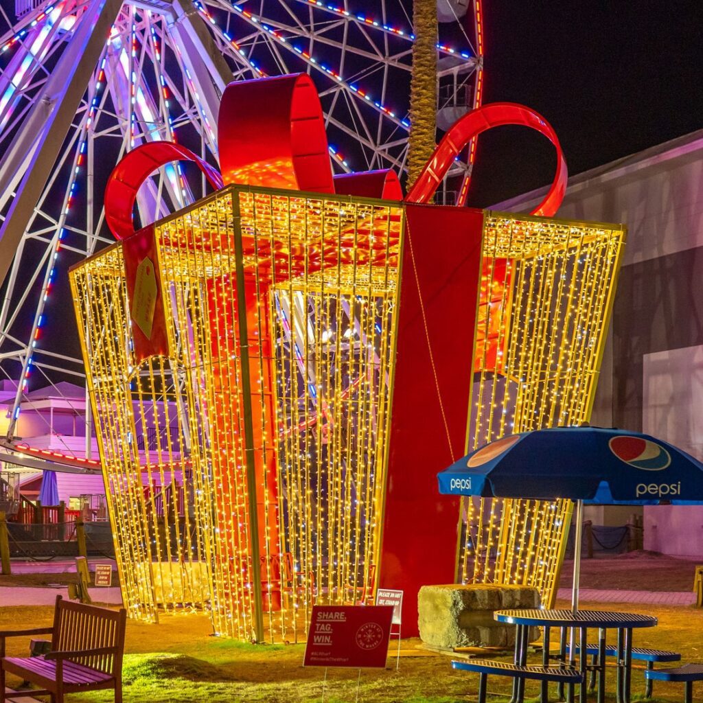 A large walk-through gift box made of yellow lights, with a big red bow, and big red ribbon.