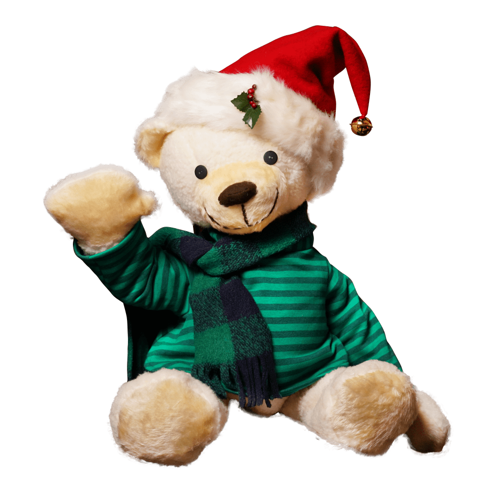 A teddy bear in a green shirt, green scarf, and Santa hat waving.
