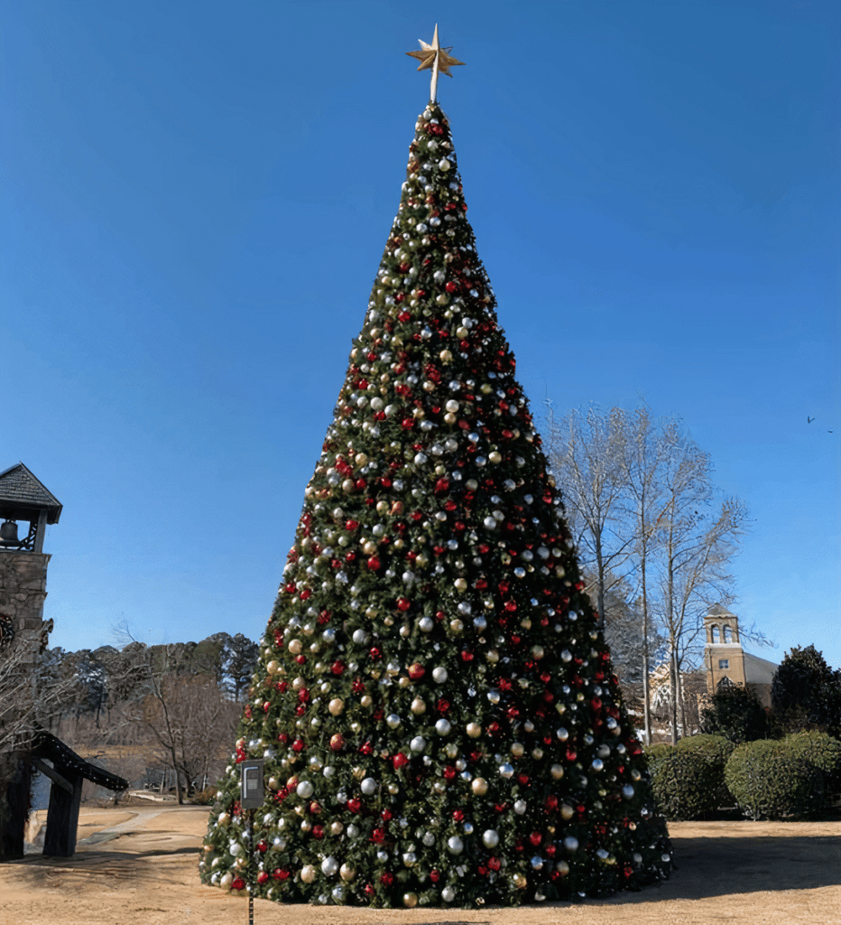 A tall Christmas tree outside with red, silver, and gold, ornaments, and warm white LED lights.