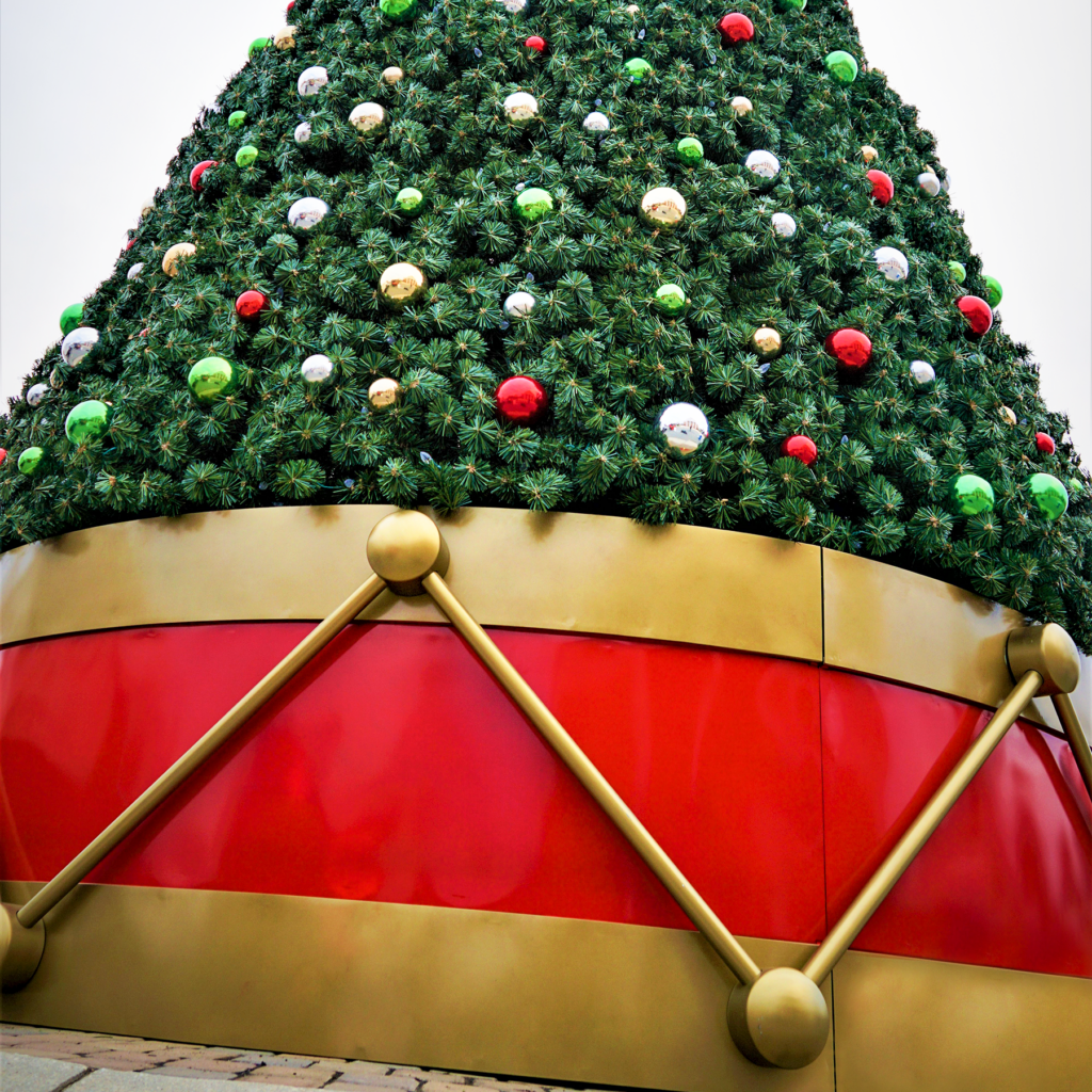 A large decorated Christmas tree sitting atop a red and gold drum.