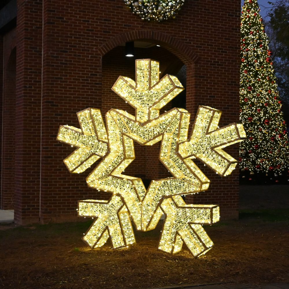 A large 3D illuminated snowflake made from gold metal, pvc mesh, and gold LED lights.