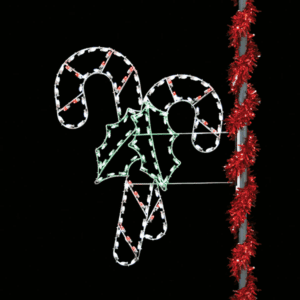 A pole mounted lit Christmas silhouette of two res and white crossing candy canes with green holly leaves in the middle.
