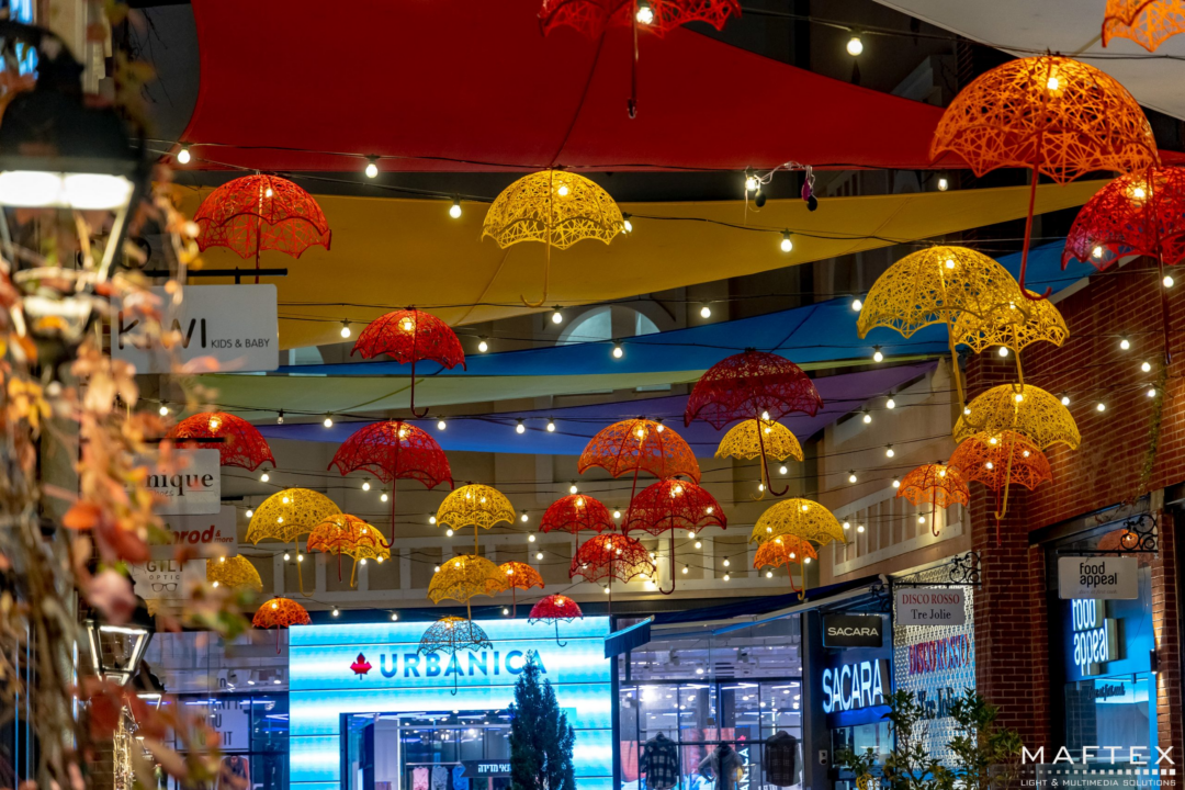 An image of an outdoor shopping center with giant red and yellow Masson fiberglass umbrellas of different sizes, hanging from above.