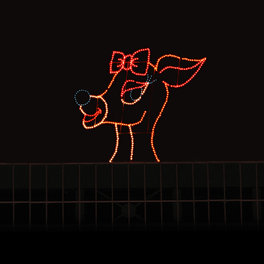 A Christmas light silhouette of a female reindeer with a bow, on top of a building.